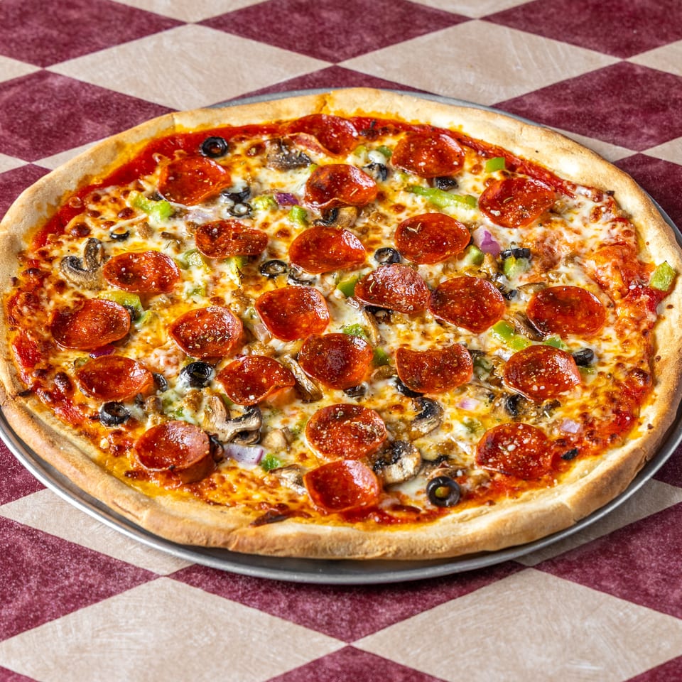 Large pepperoni pizza topped with mushrooms, black olives, green peppers, onions, and melted cheese on a metal tray.